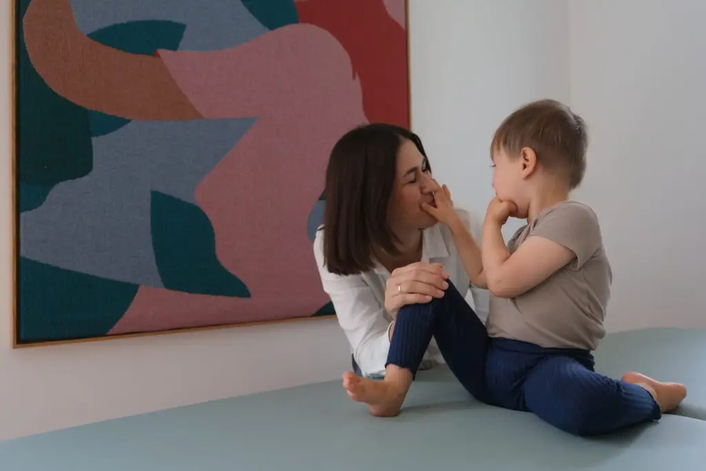 Eine Frau sitzt mit einem Kind auf einer Therapieliege und interagiert spielerisch und vertrauensvoll während einer NeuroScanBalance-Einheit.