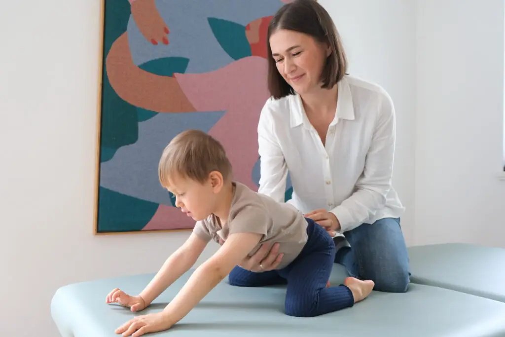 Eine Frau unterstützt ein Kind sanft bei einer NeuroScanBalance-Einheit im Vierfüßlerstand auf einer Therapieliege.